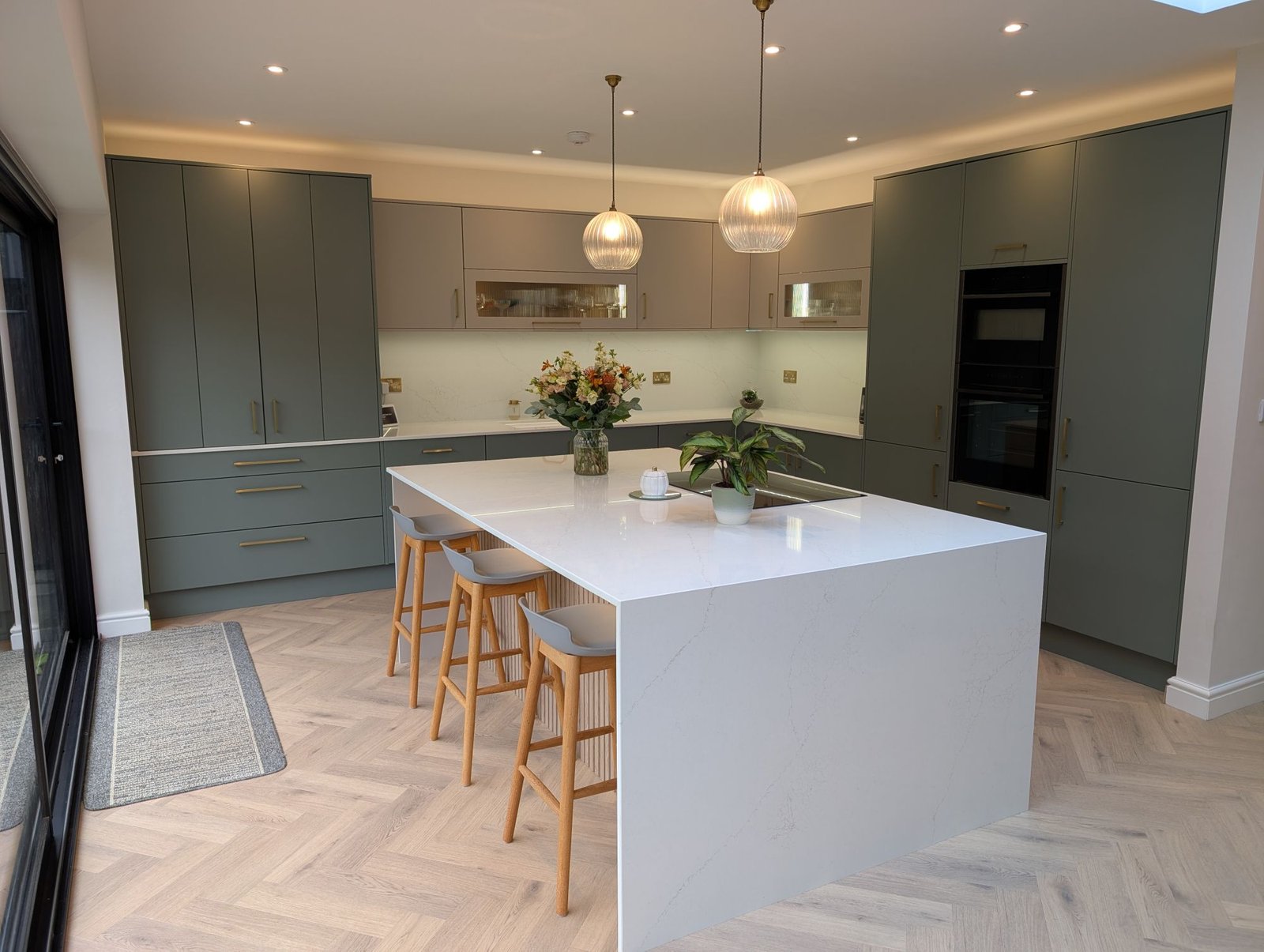 Reed Green slab-door kitchen with an Avorio Trace quartz island, breakfast stools and pendant lights
