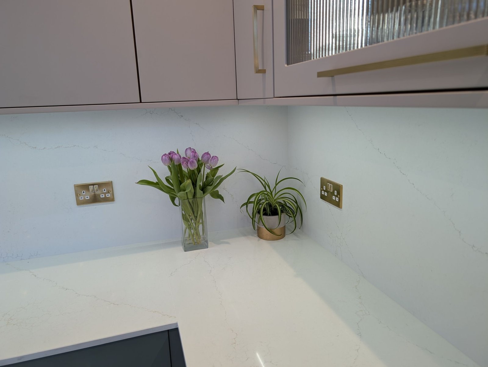 Corner of an Avorio Trace quartz worktop with full-height quartz splashback beneath Fawn wall units
