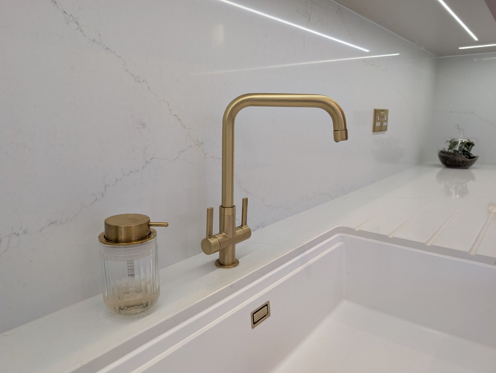 Brushed brass tap above a white undermount sink, with Avorio Trace quartz worktop and splashback