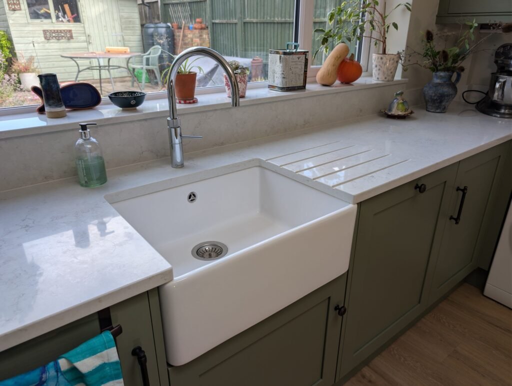 White fireclay Belfast sink with drainer grooves cut into the Chalk Mist quartz worktop and a chrome Quooker tap