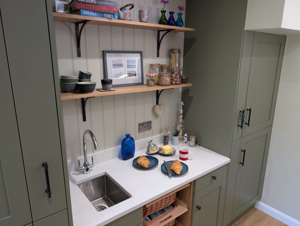 Coffee corner with a small stainless undermount sink in a Chalk Mist quartz worktop, open oak shelves and panelled wall