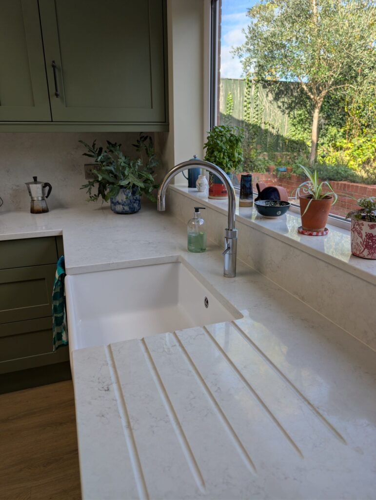 Drainer grooves in a Chalk Mist quartz worktop beside a Belfast sink and chrome Quooker tap under a garden window