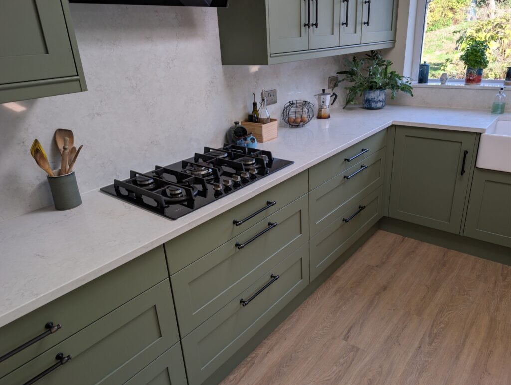 Gas hob on a Chalk Mist quartz worktop with a full quartz splashback above sage green shaker drawers