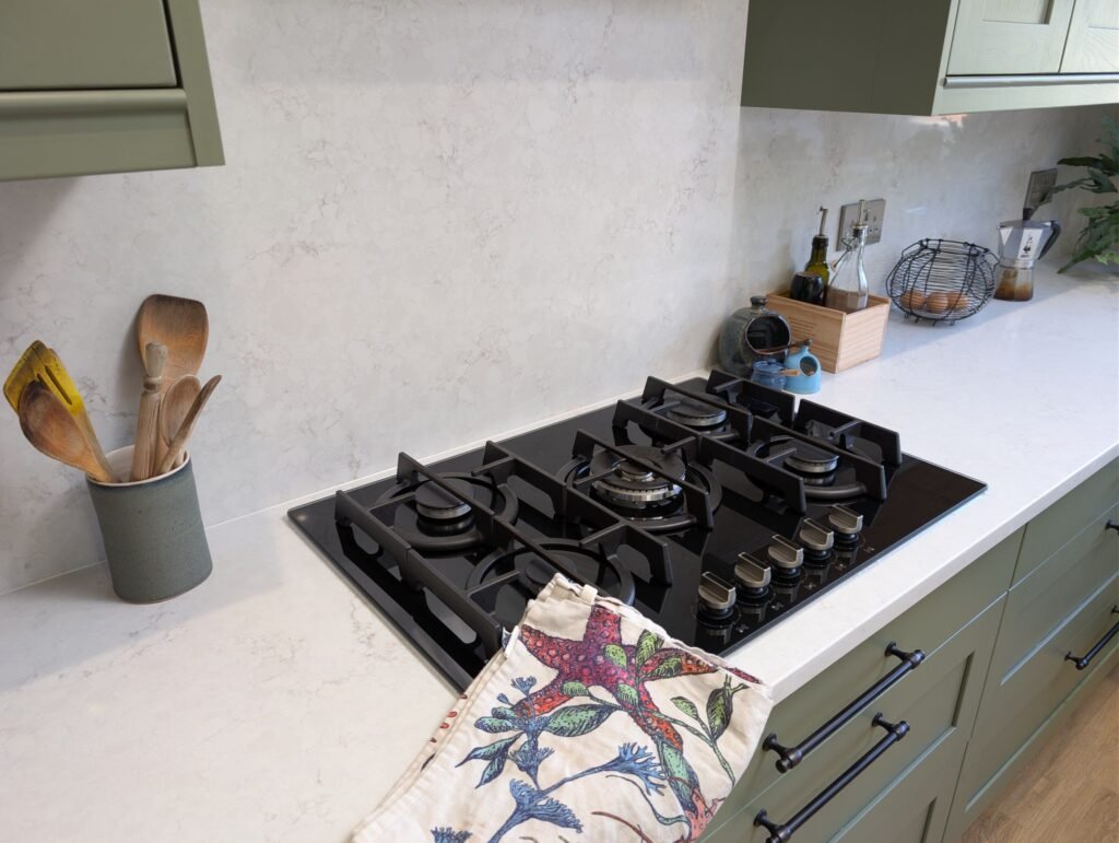 Black gas hob set into a Chalk Mist quartz worktop in front of a full-height quartz splashback