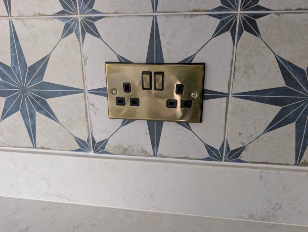 Chalk Mist quartz worktop and upstand below a blue star tile splashback with a brass double socket