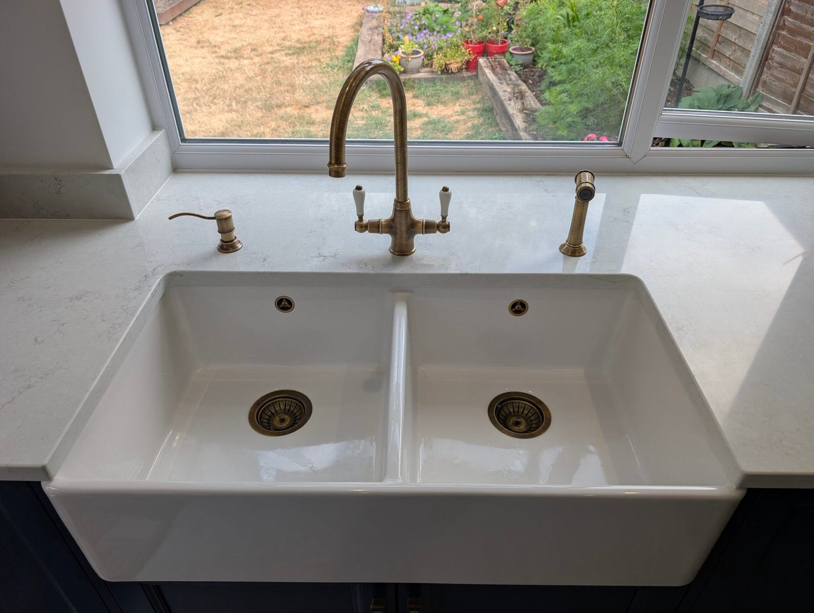 Chalk Mist quartz worktop with a white ceramic double Belfast sink and antique brass tap under a window