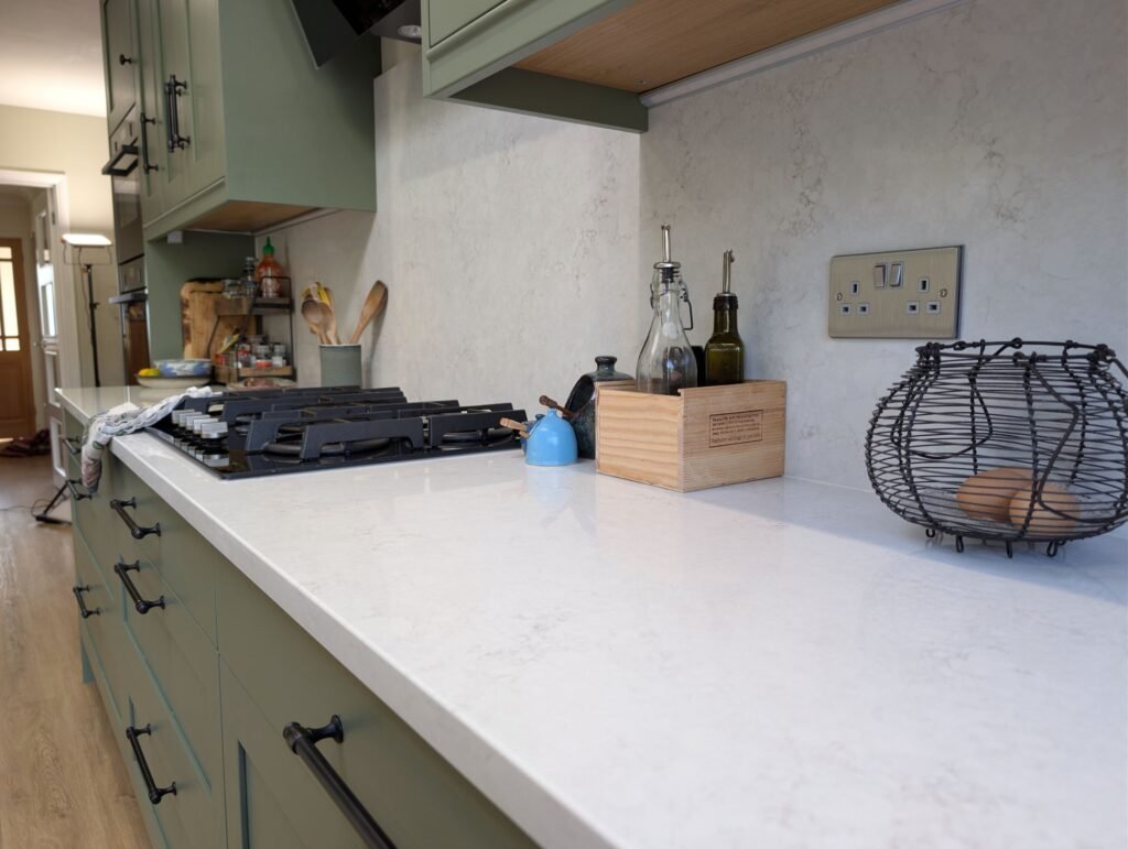 Chalk Mist quartz worktop corner with splashback, beside a gas hob and sage green shaker units