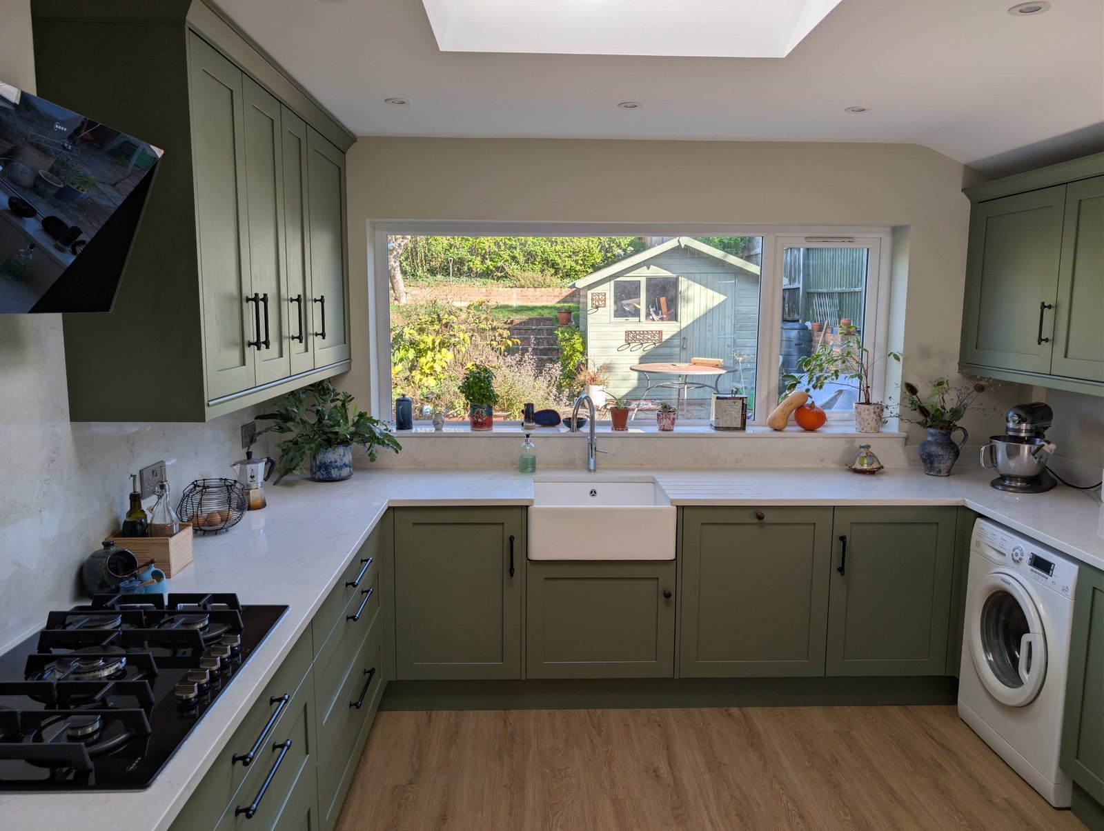 U-shaped sage green shaker kitchen with Chalk Mist quartz worktops, a Belfast sink under the window and a gas hob
