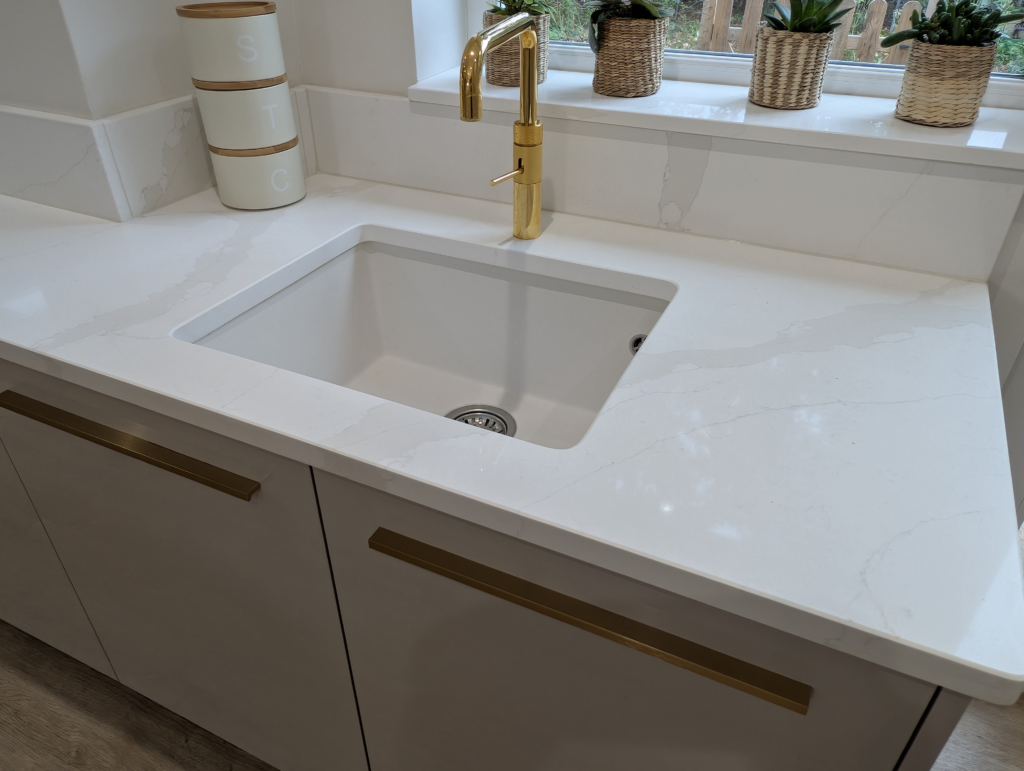 White undermount sink and brass tap set into a Gilded Vein quartz worktop with matching upstand
