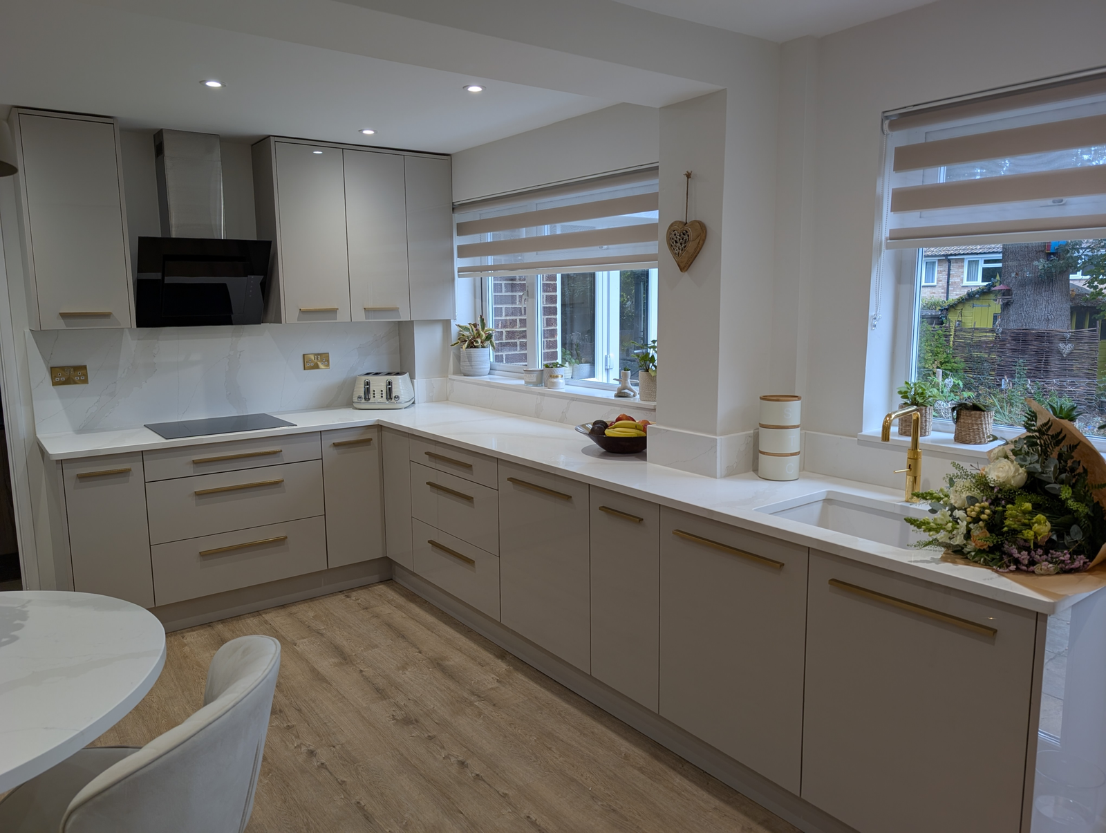 L-shaped gloss cashmere kitchen with Gilded Vein quartz worktops, full-height splashback and a teardrop quartz table