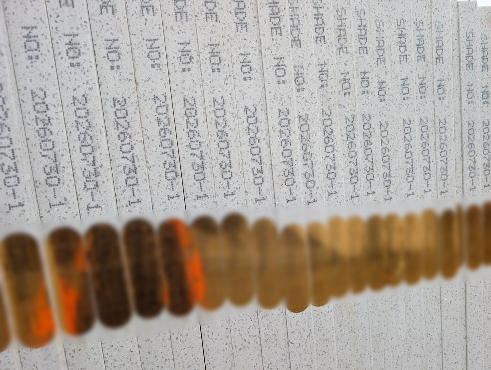 Edges of stacked low-silica quartz slabs, each stamped with a batch and shade number above a row of gold factory tags